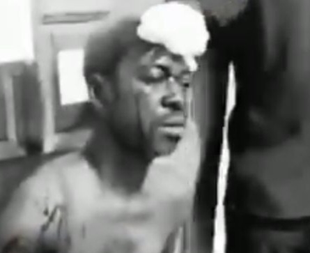 Man shirtless with a towel on his head, eyes closed, seated in a dim room.