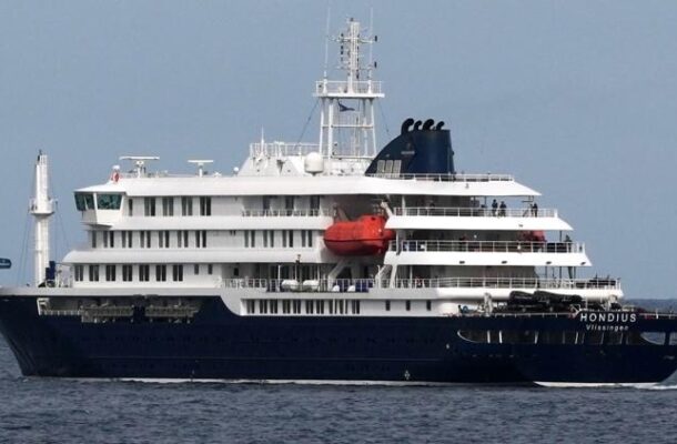 IMG-20260510-WA0032 | Ghanaguardian.com Large multi-deck cruise ship with dark blue hull and white superstructure sailing on calm open water, red lifeboat visible midship.