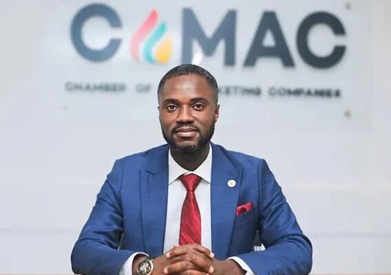 Portrait of a man in a blue suit and red tie seated at a desk with a CMAC sign behind him.