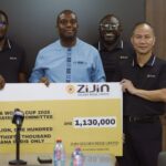 Four men stand behind a large ceremonial cheque from ZiJin Golden Ridge Limited during a press event. The sign shows an amount of GHS 1,130,000 for a Ghana World Cup 2026 fundraiser, with microphones in the foreground.
