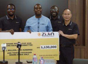 Four men stand behind a large ceremonial cheque from ZiJin Golden Ridge Limited during a press event. The sign shows an amount of GHS 1,130,000 for a Ghana World Cup 2026 fundraiser, with microphones in the foreground.