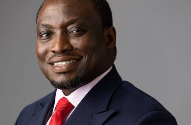 Portrait of a smiling Black businessman in a navy suit and red tie against a gray backdrop, looking at the camera.