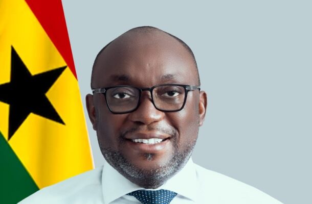 IMG-20260528-WA0001 | Ghanaguardian.com Smiling man with glasses in a white shirt and blue tie, in front of a flag with a black star (Ghana flag).
