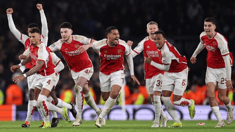 Arsenal players in red and white kits celebrate a goal on the pitch, arms raised and smiles, as teammates sprint in triumph.