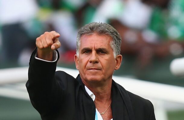 Middle-aged man in a black suit points forward with a serious expression during a sports event on the field.