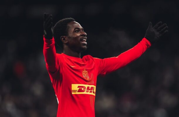 Soccer player in a red jersey raises arms in celebration on the pitch.