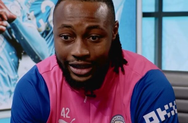 Portrait of a man with a beard and short dreadlocks, wearing a pink Manchester City jersey with blue sleeves and number 42, during an interview or discussion.