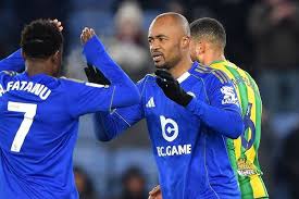 Two soccer players in blue uniforms celebrate on the field, one raising a fist toward his teammate in a congratulatory gesture.