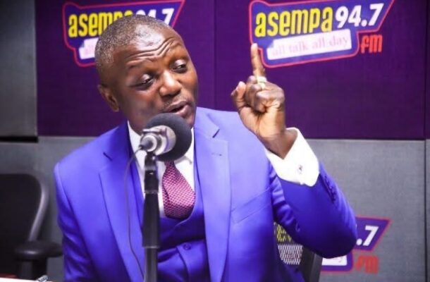 IMG_0347 | Ghanaguardian.com Man in a bright blue suit speaks into a microphone during a radio show at Asempa 94.7 studio, gesturing with one finger raised.