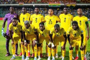 Ghana national football team lineup in yellow jerseys on the field before a match, goalie in purple seen at left.