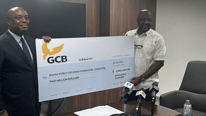 Two men in a conference room hold a large ceremonial check from GCB Bank for two million dollars.
