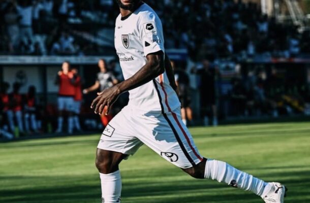 IMG_0372 | Ghanaguardian.com Soccer player in a white kit sprinting on a sunlit green field with a blurred crowd in the stands behind.