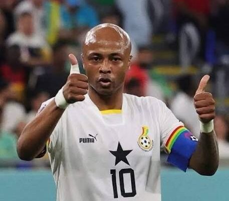 Soccer player in a white jersey with number 10 and a black star, giving two thumbs up with a rainbow captain's armband on the left arm.