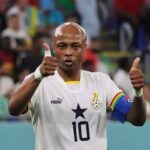 Ghana national football team player wearing number 10, giving two thumbs up with captain's armband on his left arm in a stadium.