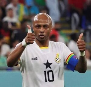 Ghana national football team player wearing number 10, giving two thumbs up with captain's armband on his left arm in a stadium.