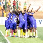 Soccer players in purple uniforms huddle together on the field in celebration.