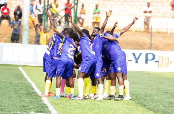 Soccer players in purple uniforms huddle together on the field in celebration.