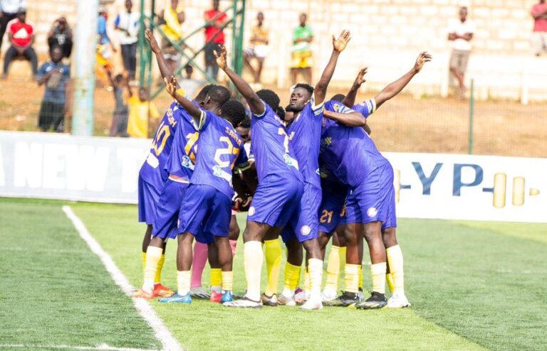 Soccer players in purple uniforms huddle together on the field in celebration.