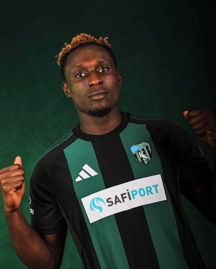Portrait of a male footballer wearing a black and green striped jersey with SAFIPORT sponsor, fists raised in a confident pose.