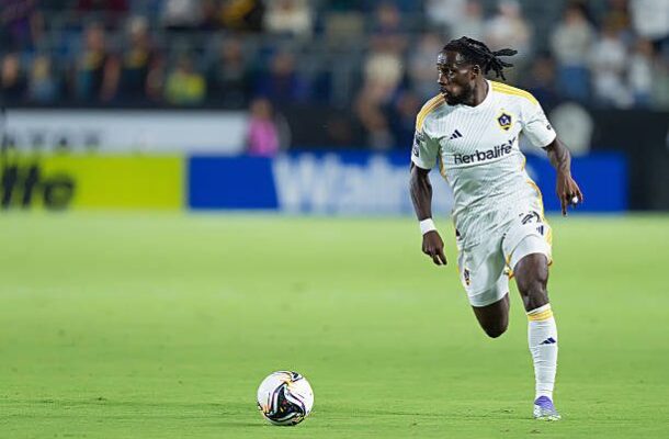 Soccer player in a white LA Galaxy kit dribbling the ball on a green field during a match