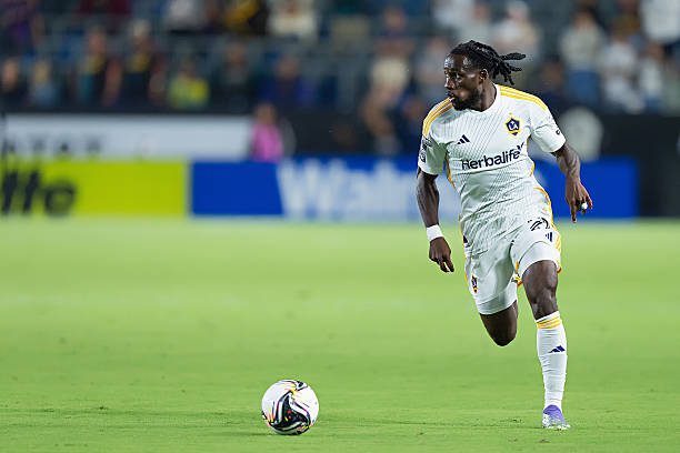 Soccer player in a white LA Galaxy kit dribbling the ball on a green field during a match