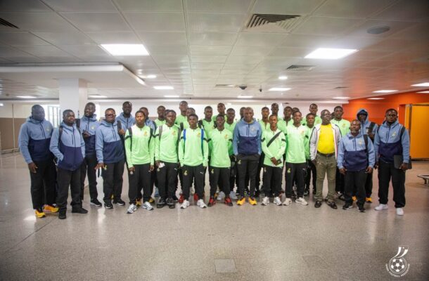 Group of young men in matching green shirts and blue jackets posing in a hallway, likely a sports team photo.