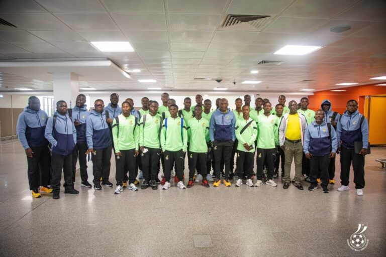 Group of young men in matching green shirts and blue jackets posing in a hallway, likely a sports team photo.