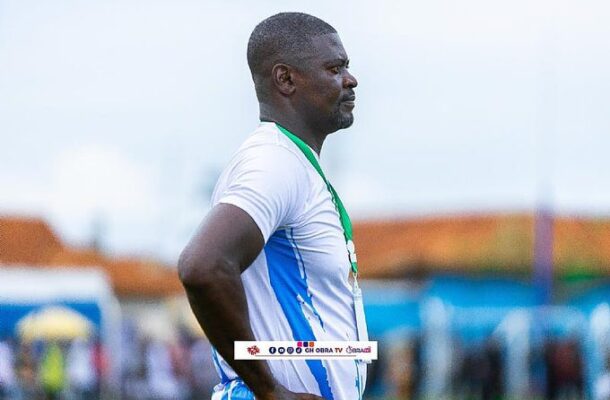 Male athlete in a white and blue jersey, with a green medal lanyard, stands in profile with hands on hips at an outdoor sports event.