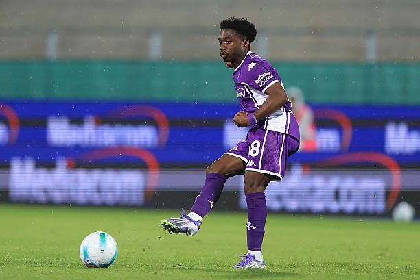 Soccer player in a purple kit kicking a ball on a rain-soaked field during a match without a visible crowd in the background.— Informative action description