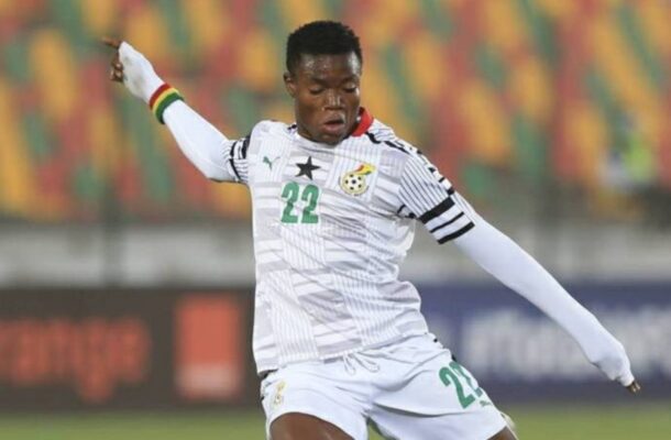 Soccer player in a white kit with number 22 mid-kick on a stadium field with colorful empty stands behind him.