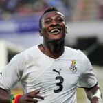 Soccer player in a white jersey with the number 3 celebrates with a smile on the field.