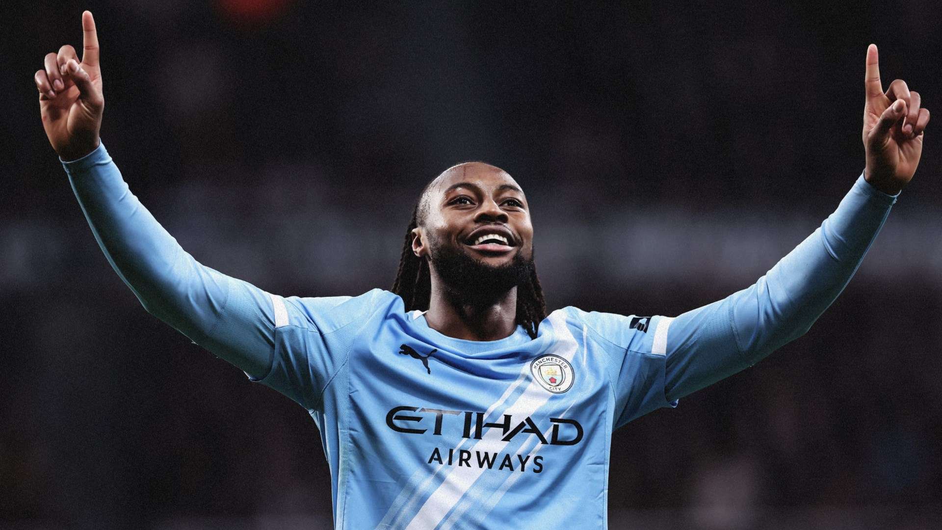 Footballer in Manchester City kit with arms raised in celebration on the pitch.