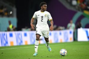 Ghana national team player in a white kit with number 2 dribbling the ball on a green pitch during a match.