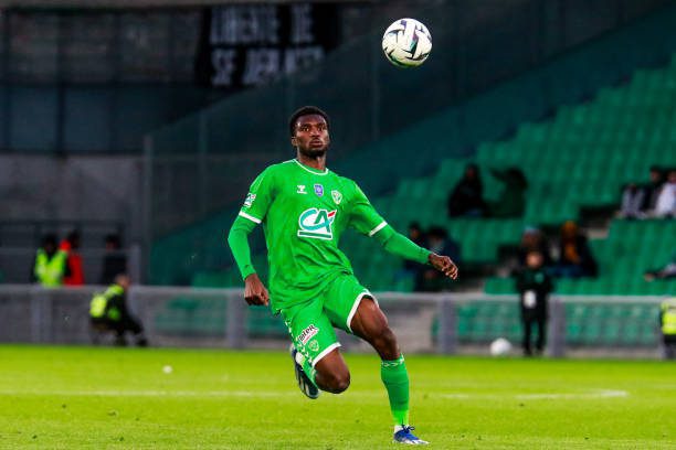 Soccer players in a green kit on a grass field, ball in the air as it approaches during a night match.