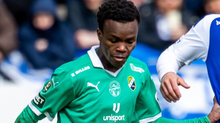 Soccer player in a green jersey with sponsor and club badges, focused on the ball during a match.