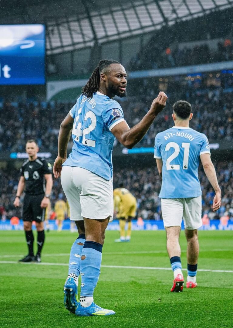 Two Manchester City players celebrate on a rainy pitch, foreground player raising a fist (#42).