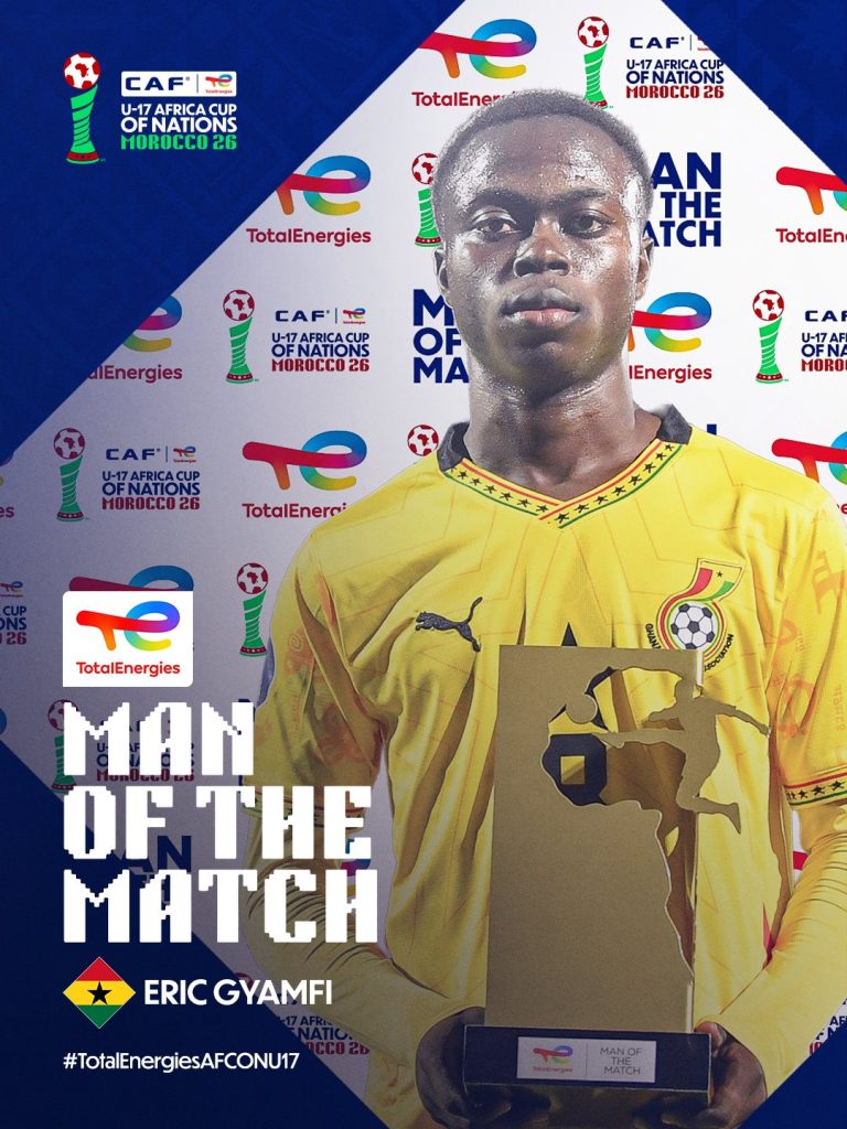 Eric Gyamfi in a yellow jersey holding the Man of the Match trophy at a sponsor backdrop.