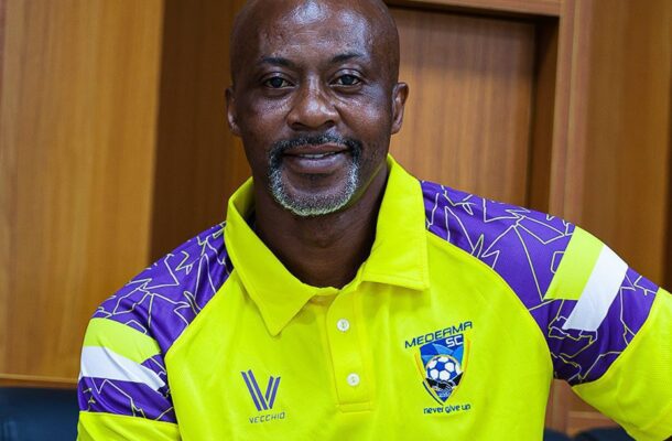 Smiling man in a neon yellow and purple soccer jersey, indoors, facing the camera.