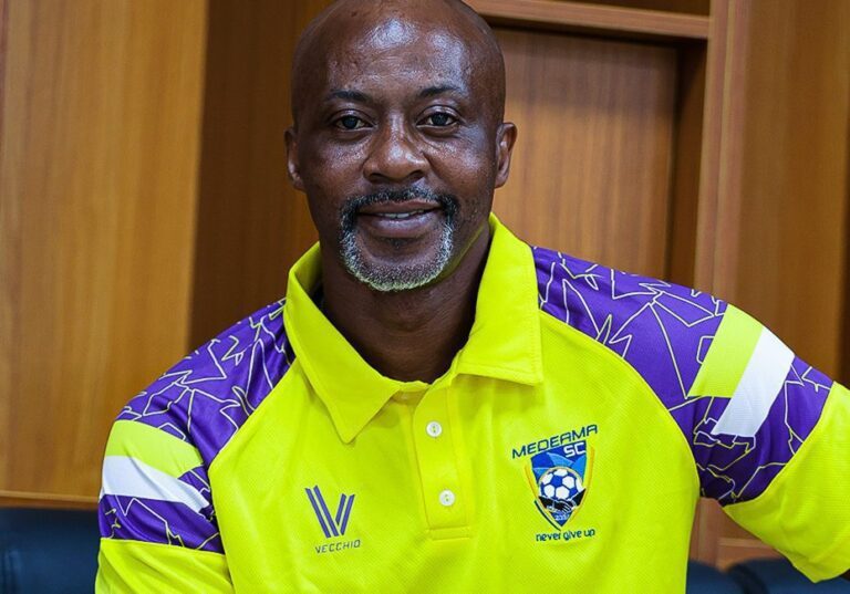 Smiling man in a neon yellow and purple soccer jersey, indoors, facing the camera.