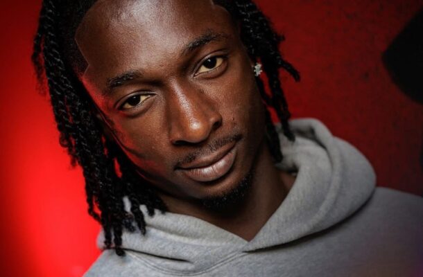 Portrait of a man with dreadlocks wearing a gray hoodie against a red backdrop; 'FIRST PRO CONTRACT' logo and 'Elisha Boateng' text visible.