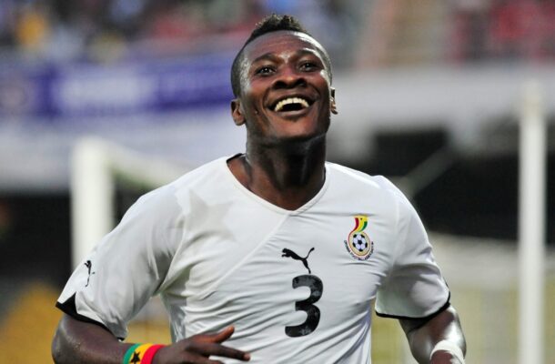 Football player in a white jersey celebrating, smiling during a match with Senegal crest visible on chest and a rainbow wristband.