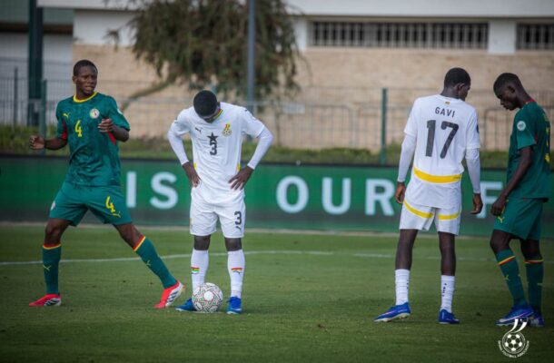 Soccer players on a grassy field: a player in white jersey number 3 stands over a ball, flanked by players in green uniforms during a match.