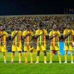 Senegal national football team in yellow kits stands in a line on the field with hands over their hearts before a match.