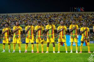 Senegal national football team in yellow kits stands in a line on the field with hands over their hearts before a match.