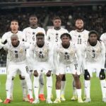 Ghana national football team lineup posing for a pre-match photo in white kits on a green pitch.