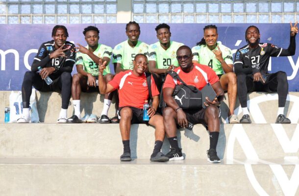 Group of soccer players and two staff members sit on stadium steps, posing for a photo in green jerseys and red shirts.