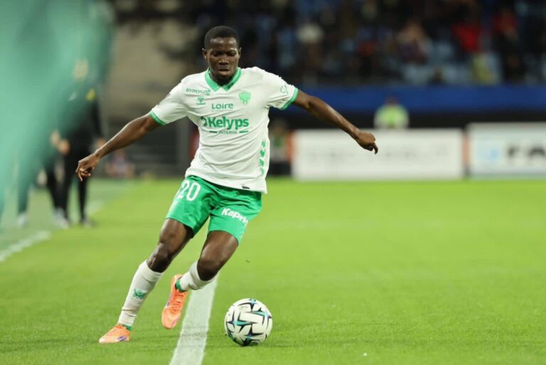 Soccer player in white and green kit controls the ball on a grass field during a match, number 20 visible on shorts