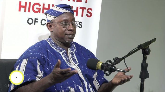 Man in blue traditional clothing speaking into a microphone at a press event, banner behind him reads 'HIGHLIGHTS'.