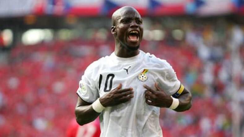 Football player in a white jersey with number 10 celebrates a goal, hands on chest, shouting with joy on the field.