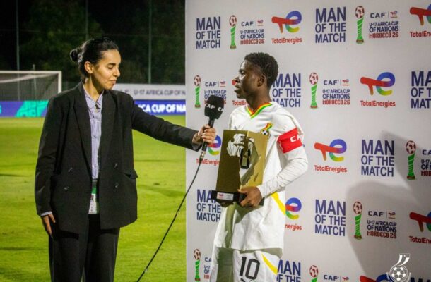 IMG_0619 | Ghanaguardian.com Reporter interviews a soccer player in a white jersey with a trophy on a podium backdrop that reads 'Man of the Match'.